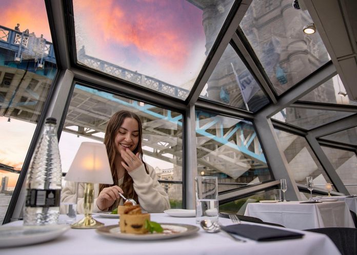 Jeune femme mangeant un gâteau sur un bateau qui passe sous le pont de Tower Bridge à Londres